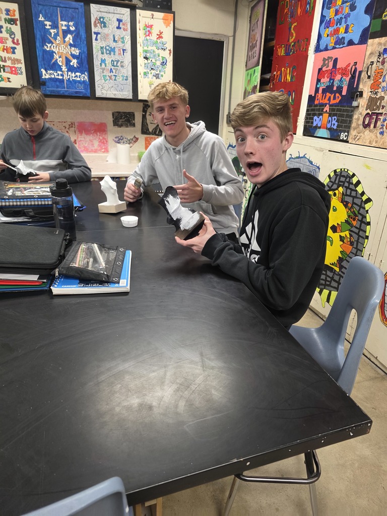 Two students are painting their sculptures. One is black and the other is white.