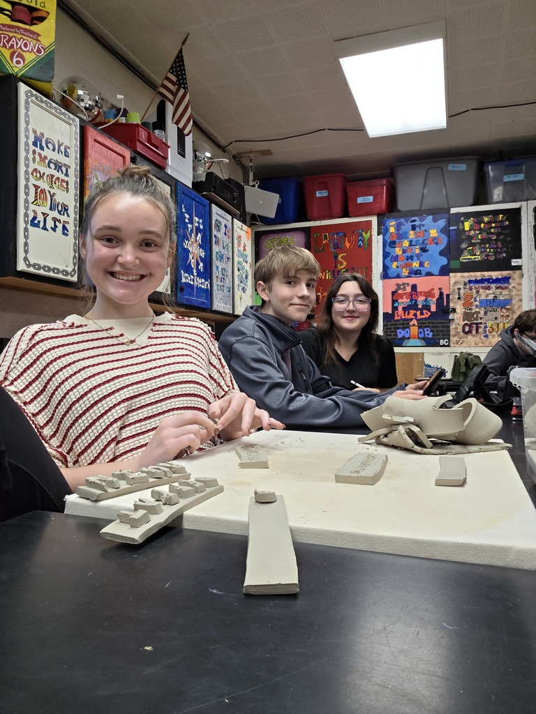 Three students are molding clay into a design.
