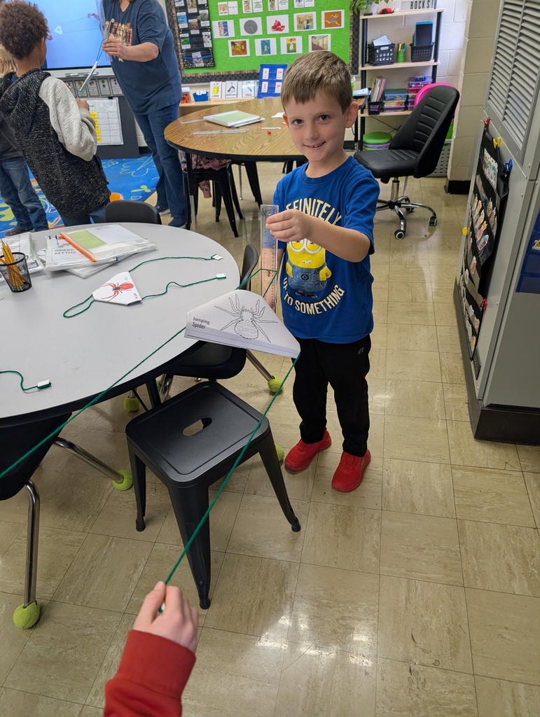 A student is moving the spider along the yarn "web" towards the secoond student. 