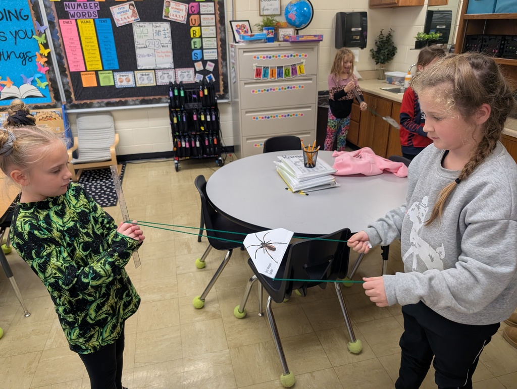 A student is moving the spider along the yarn "web" towards the secoond student. 
