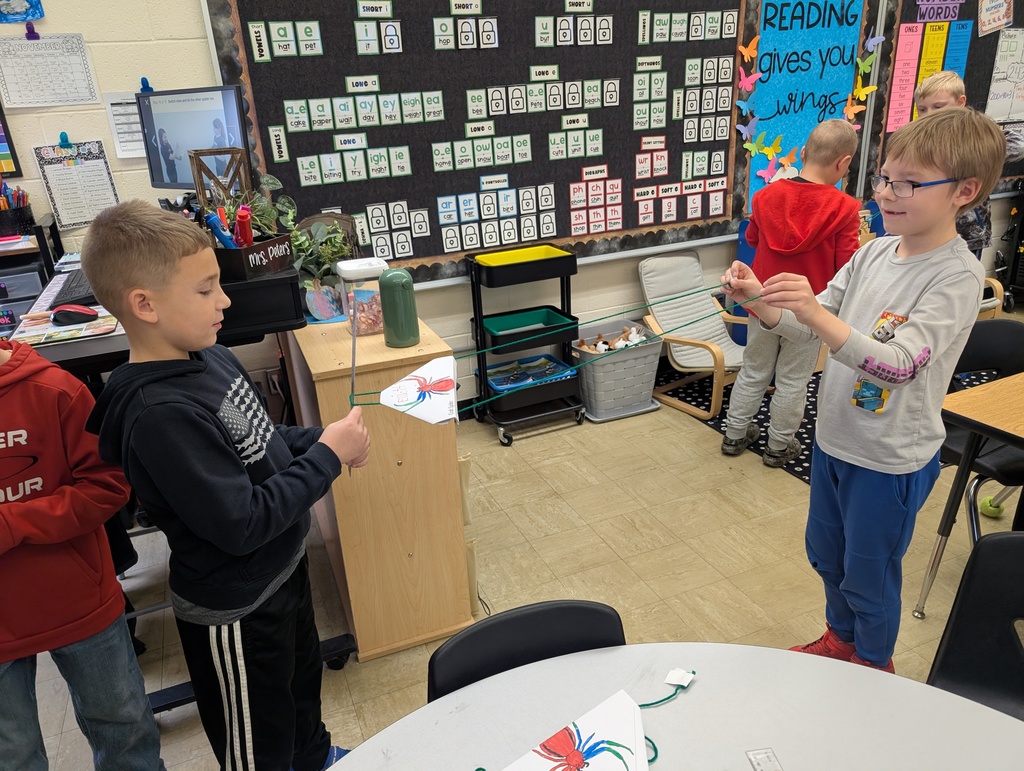 A student is moving the spider along the yarn "web" towards the secoond student. 