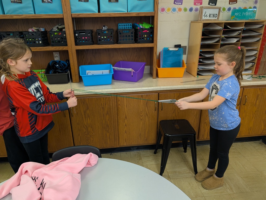 A student is moving the spider along the yarn "web" towards the secoond student. 