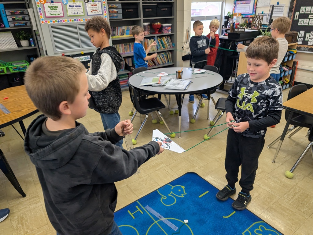 A student is moving the spider along the yarn "web" towards the secoond student. 