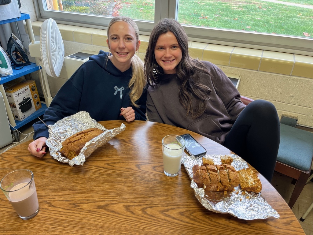 Two students are sitting at the table. They have two loaves of bread opened and have glasses of milk.