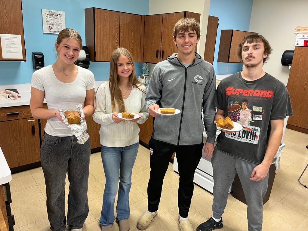 Four students are standing together. They are each holding some pumpkin bread. 
