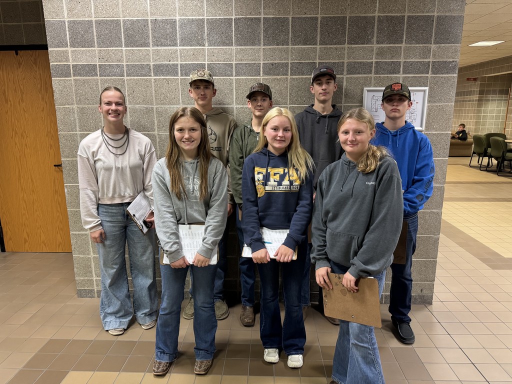 The group of eight students are standing together. They are each holding a clipboard. 