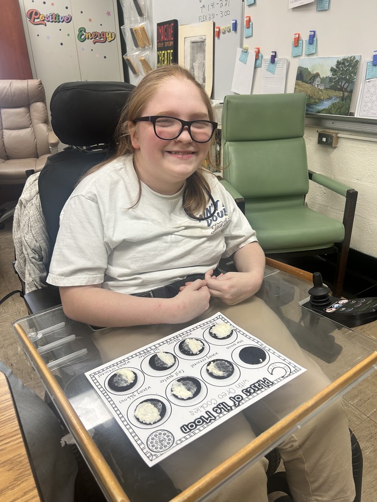 A student is sitting at the desk. The paper with oreo phases of the moon are shown on the desk. 