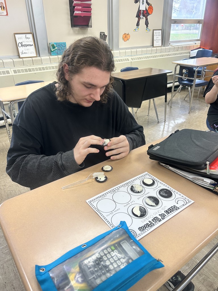 A student is sitting at the desk. The paper with oreo phases of the moon are shown on the desk. 