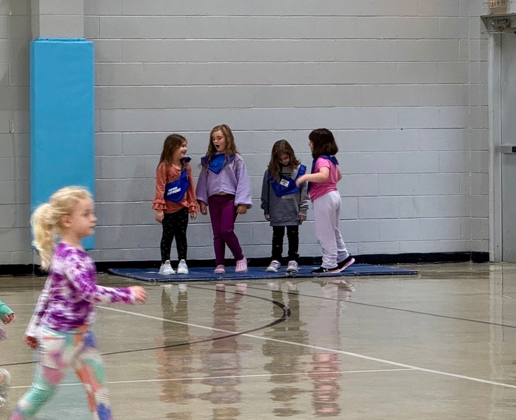 Four sutdents are standing on a haystack, a mat in the corner of the gym. 