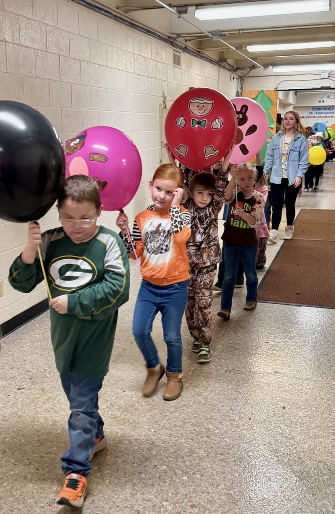 The students are parading through the hallways. They are holding their balloons up for everyone to see. The balloons are decorated in animal designs. 