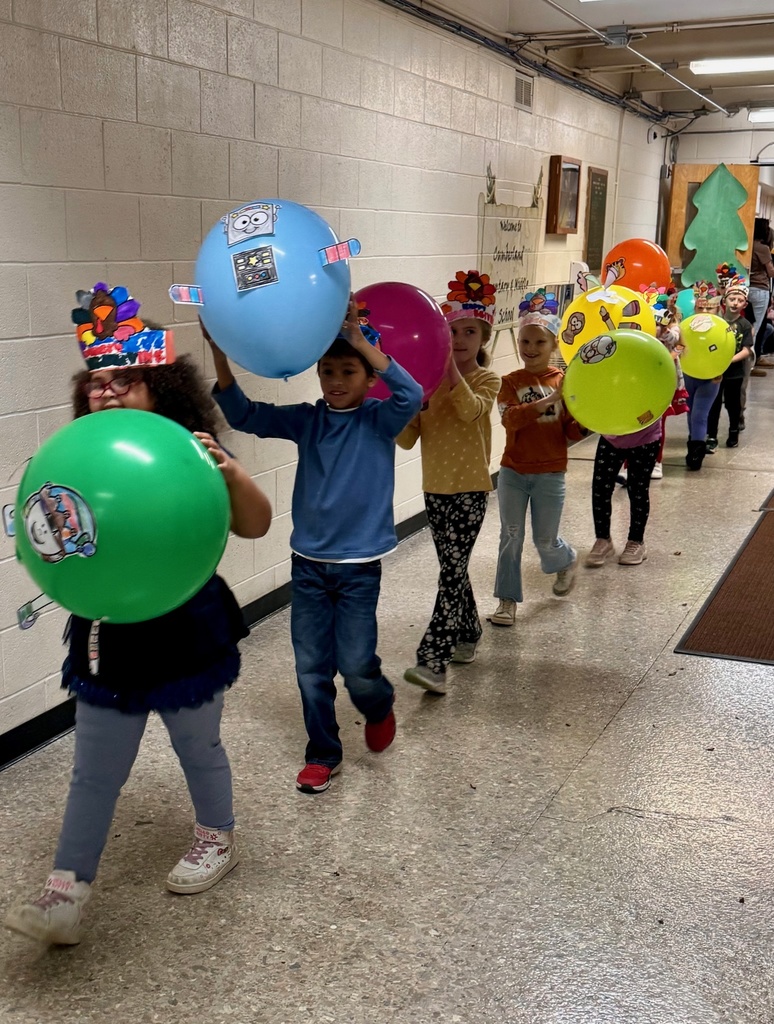 The students are parading through the hallways. They are holding their balloons up for everyone to see. The balloons are decorated in animal designs. 