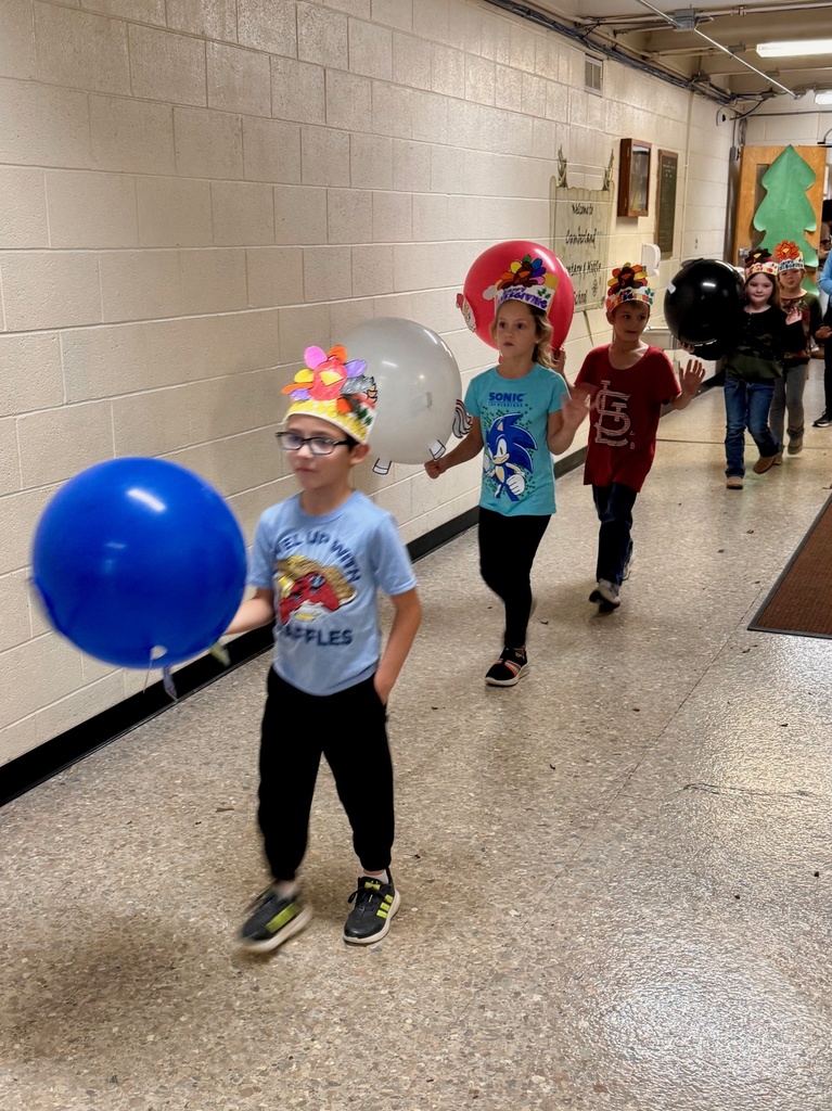 The students are parading through the hallways. They are holding their balloons up for everyone to see. The balloons are decorated in animal designs. 