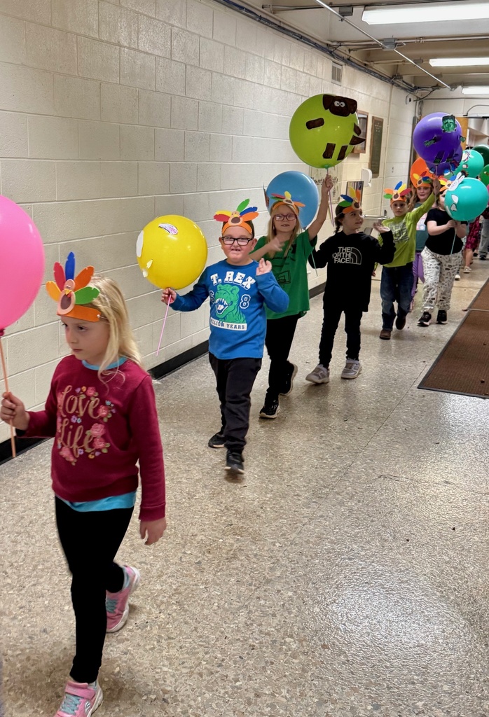 The students are parading through the hallways. They are holding their balloons up for everyone to see. The balloons are decorated in animal designs. 