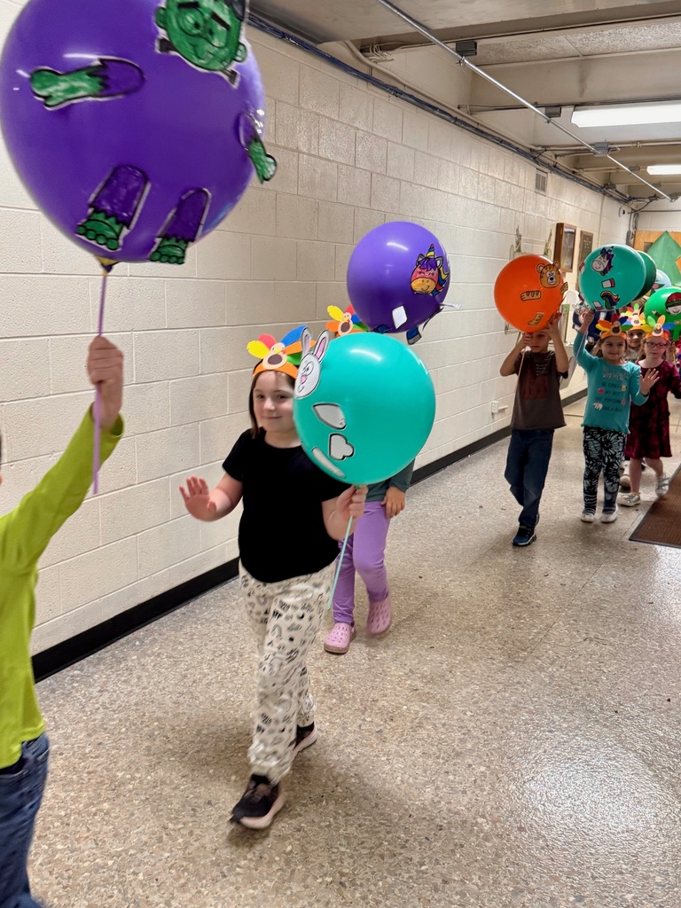 The students are parading through the hallways. They are holding their balloons up for everyone to see. The balloons are decorated in animal designs. 
