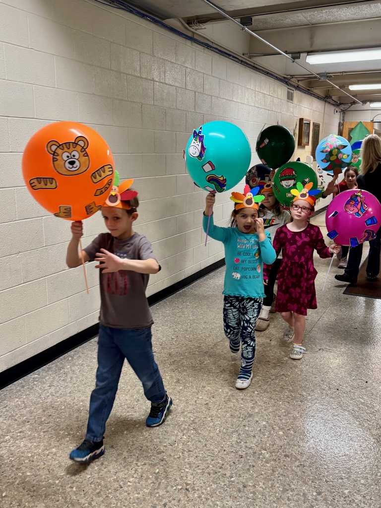 The students are parading through the hallways. They are holding their balloons up for everyone to see. The balloons are decorated in animal designs. 