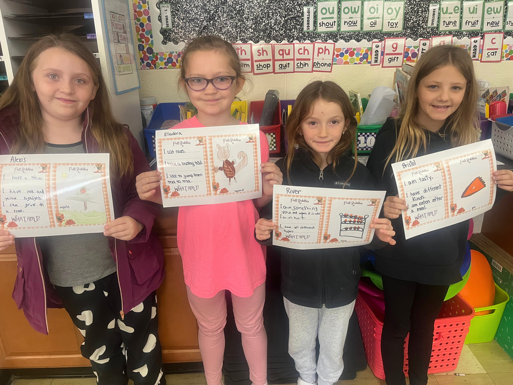 Students are standing side by side. They are holding up their riddles and the picture that goes with it.