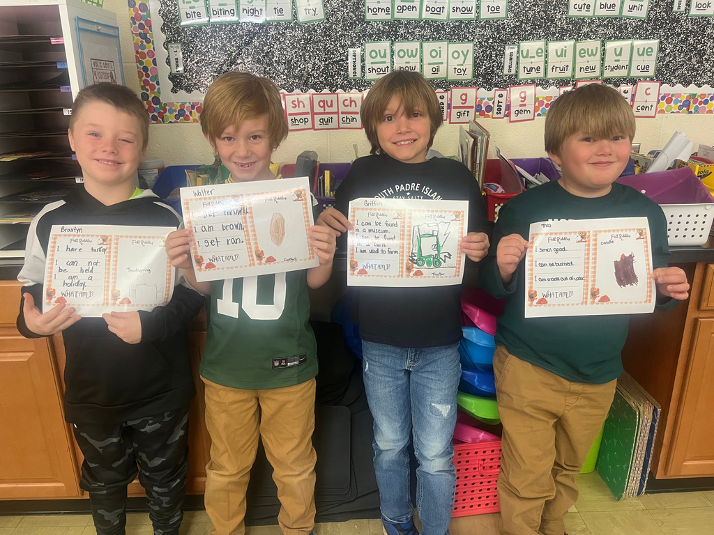 Students are standing side by side. They are holding up their riddles and the picture that goes with it.