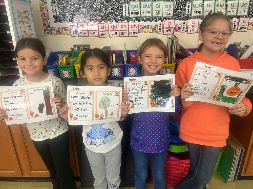 Students are standing side by side. They are holding up their riddles and the picture that goes with it.