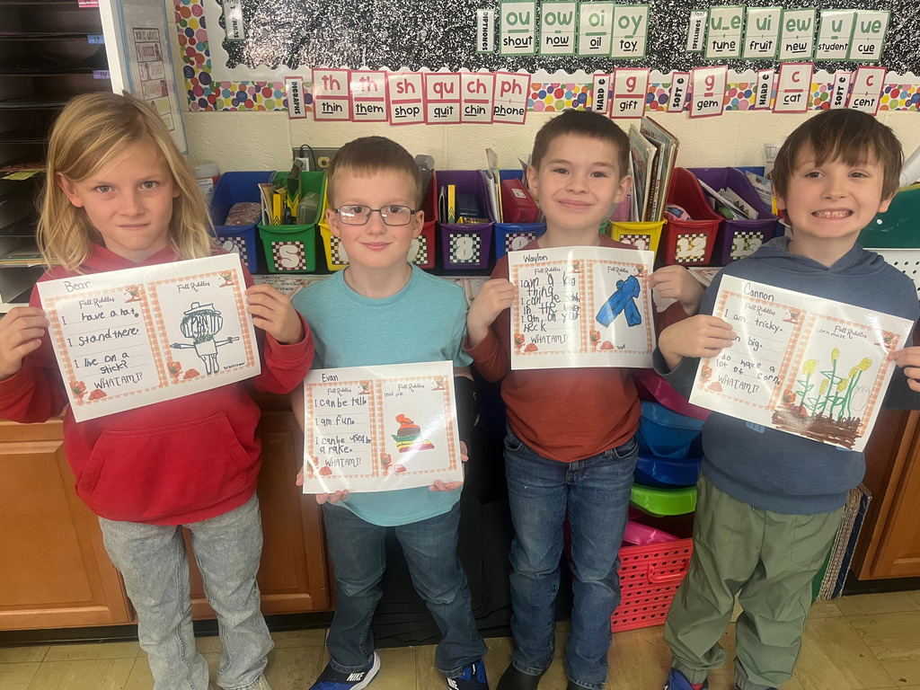 Students are standing side by side. They are holding up their riddles and the picture that goes with it.