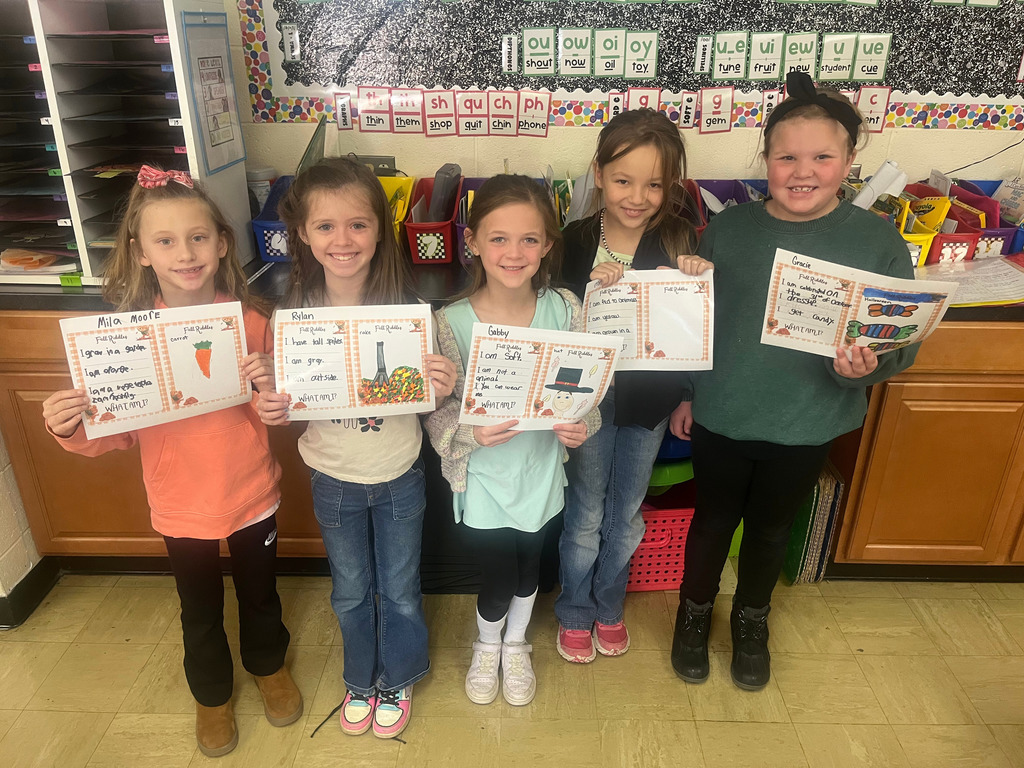 Students are standing side by side. They are holding up their riddles and the picture that goes with it.