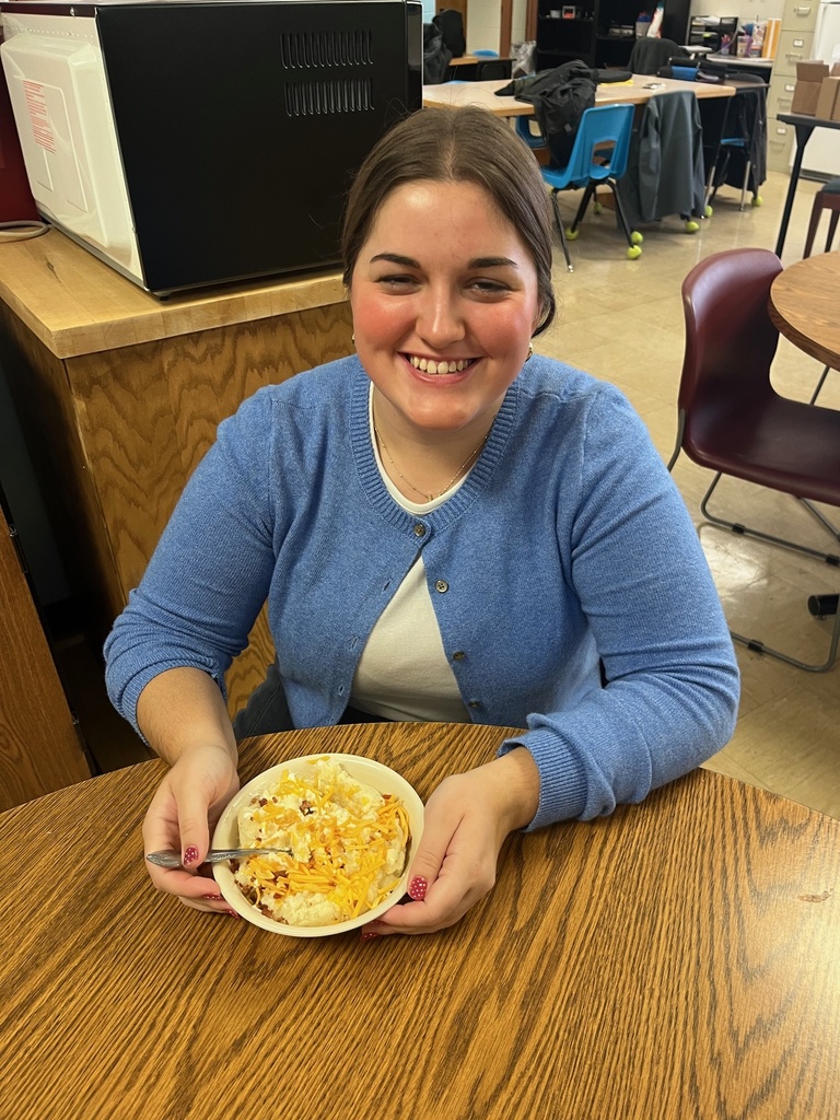 A student is sitting at a table with a bowl of loaded mashed potatoes. 