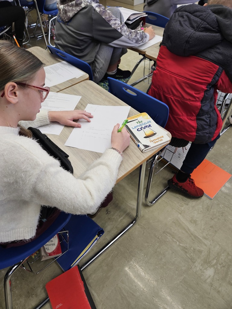 A student is sitting at a desk. She is writing a poem. 