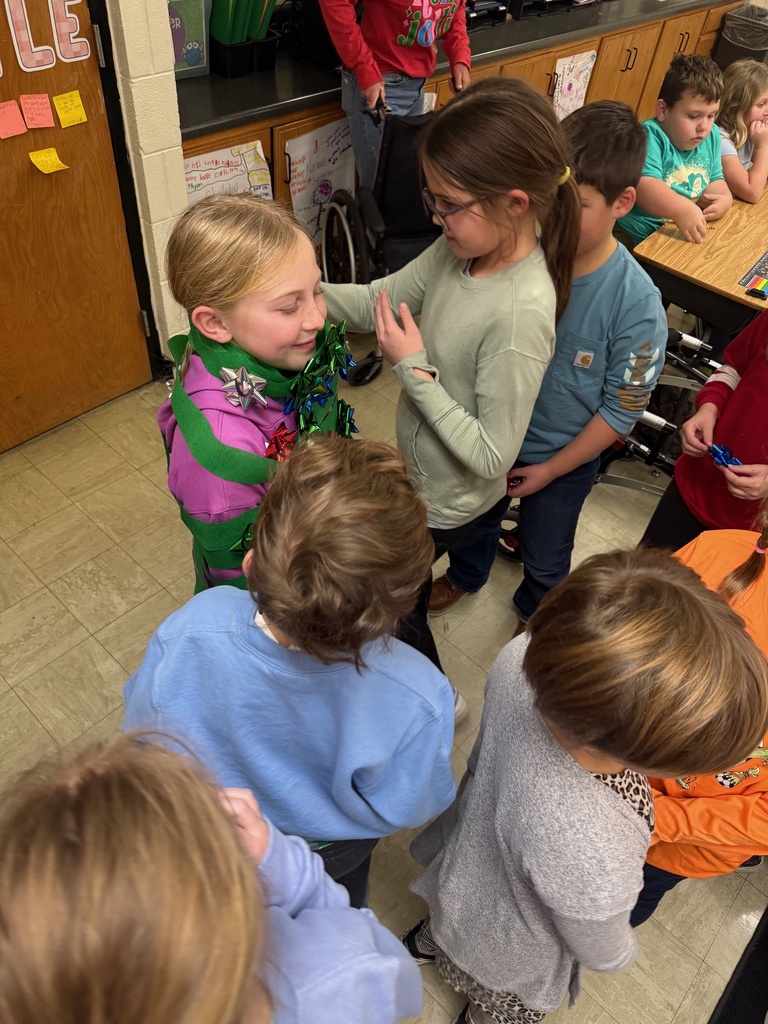 The students are in a line to add an ornament (a bow) to the Christmas tree (student).