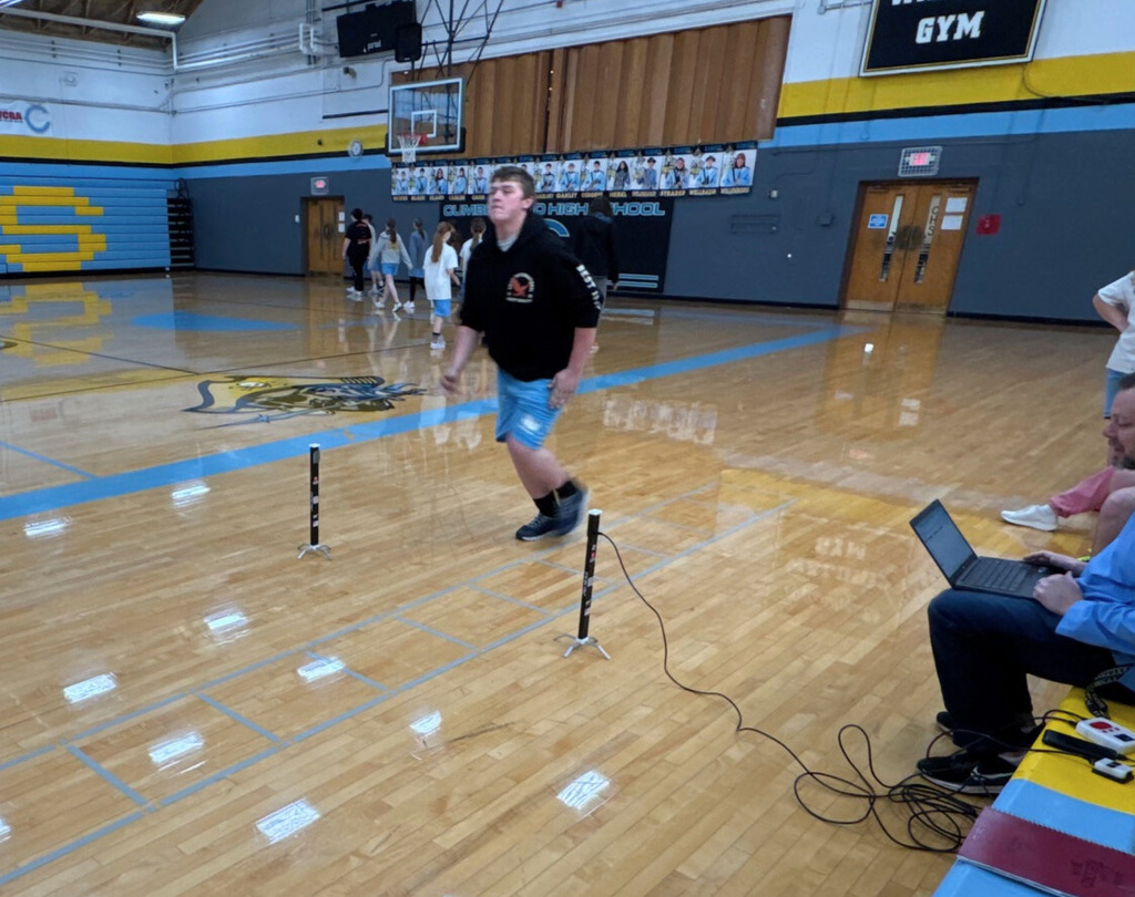 The student is running a portion of the shuttle run. The student is running between two sensors to one end of the run. 