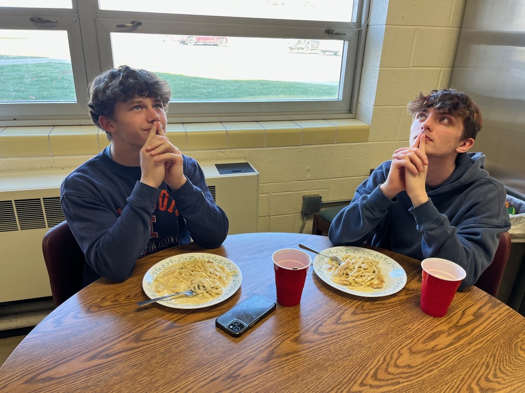 Two students are sitting in front of their chicken alfredo. They are clasping their hands and looking upward.