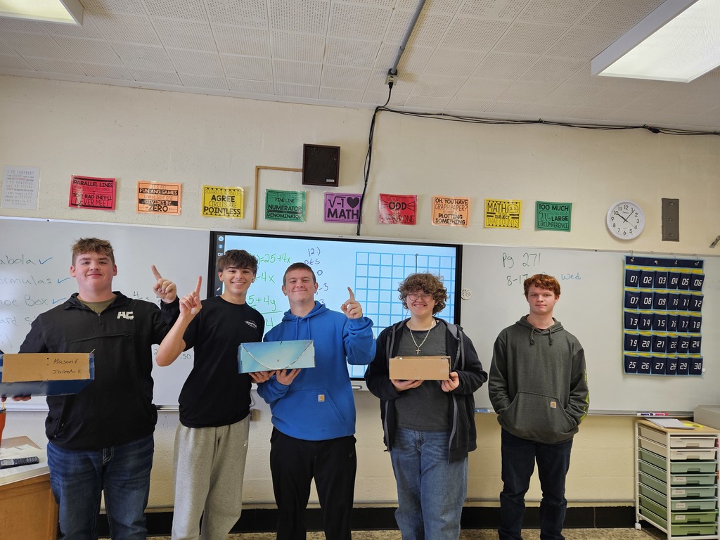 The students in the class are holding their shoebox ovens. Three students are holding up the number one sign.
