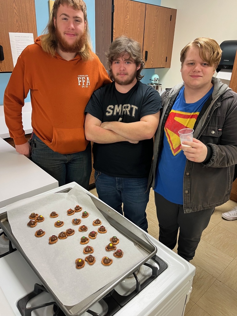 Students are standing in front of the oven with their batch of holiday pretzels. The pretzels have a hershey's kiss and m&m on top.