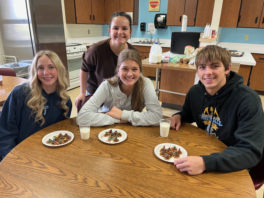 Students are at the table with their batch of holiday pretzels. The pretzels have a hershey's kiss and m&m on top.