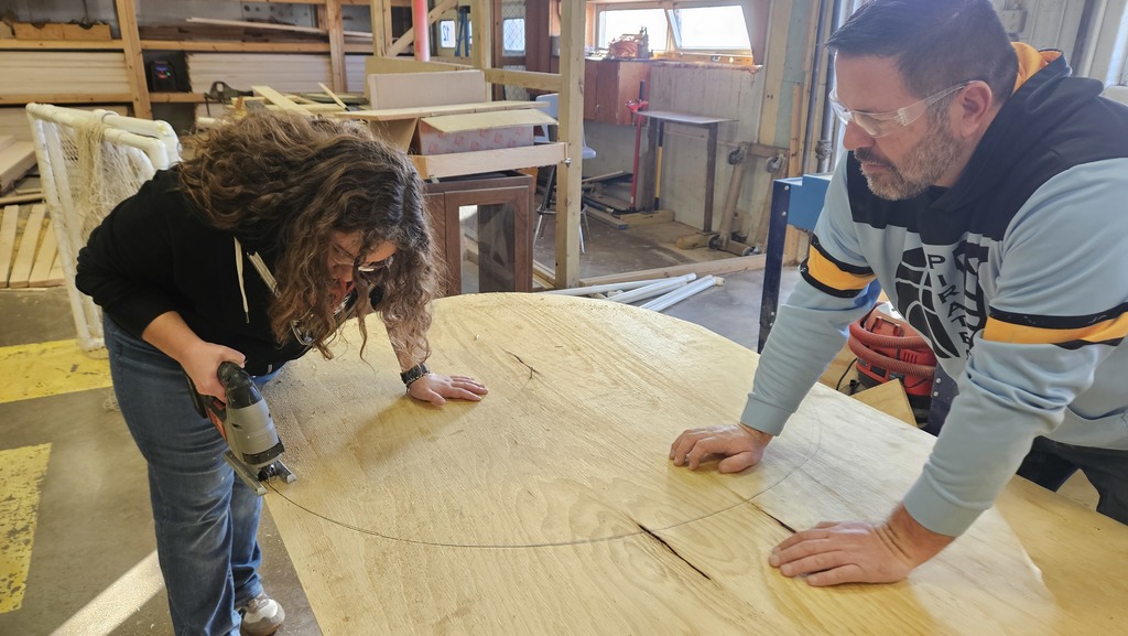A student is sawing the plywood into a circle.