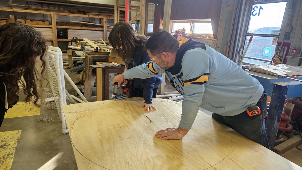 A teacher is showing a student how to cut a circle in the plywood.