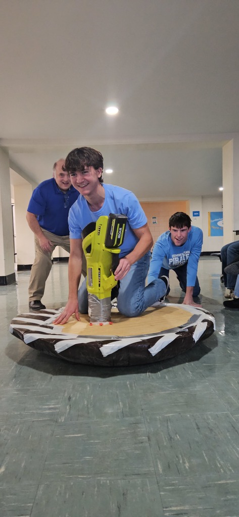 A student is riding the hovercraft. Two people are standing in the back for support.