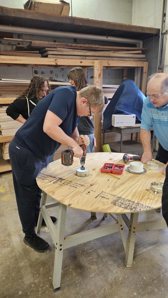 A teacher is observing a student cut a circle hole into the plywood.