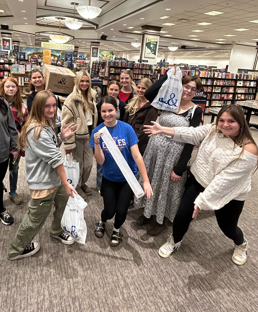 A group of ten students are holding all of the purchased books. They are in bags and boxes. One student is holding the long receipt. 