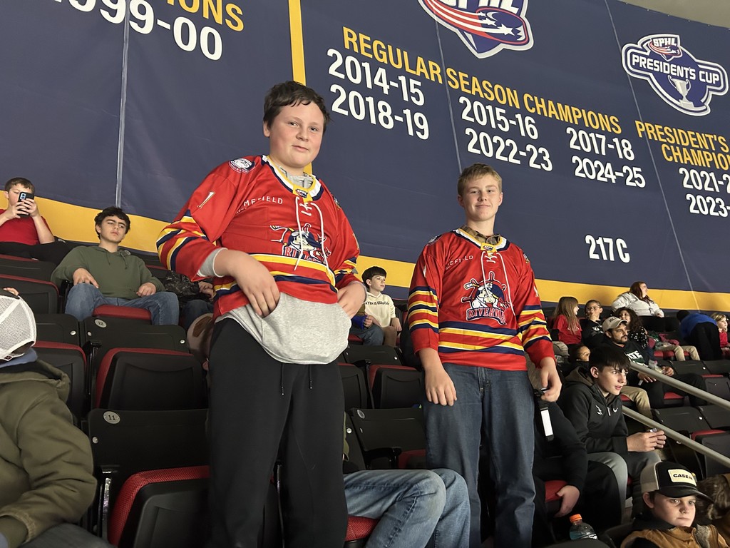 Two students are standing wearing a Rivermen jersey. 