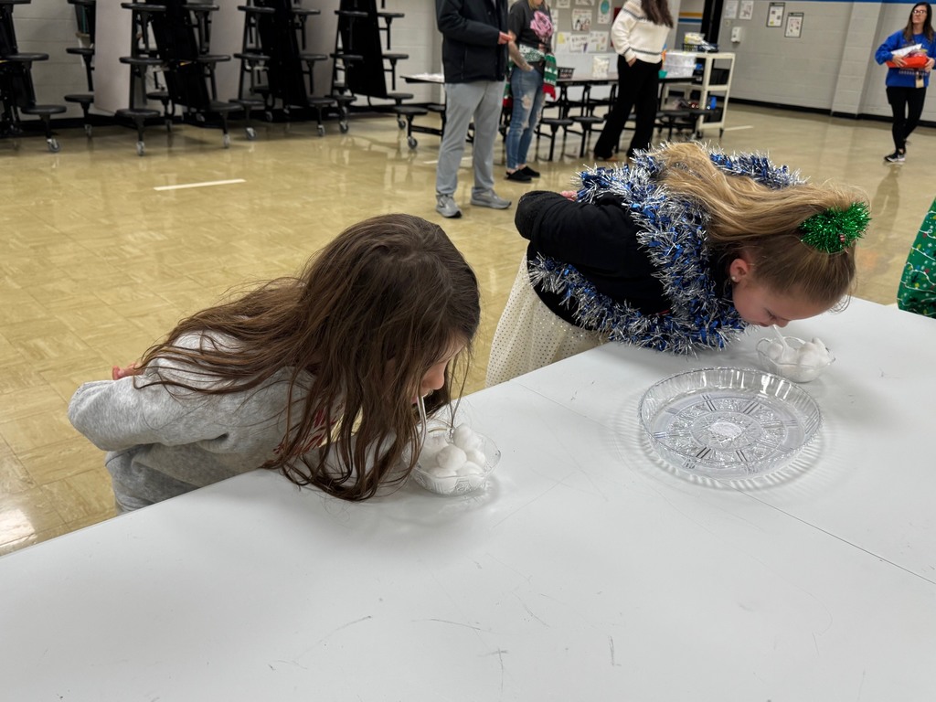 Students have a spoon in their mouths. They have to move the cotton balls from one dish to the other using only the spoon and no hands. 