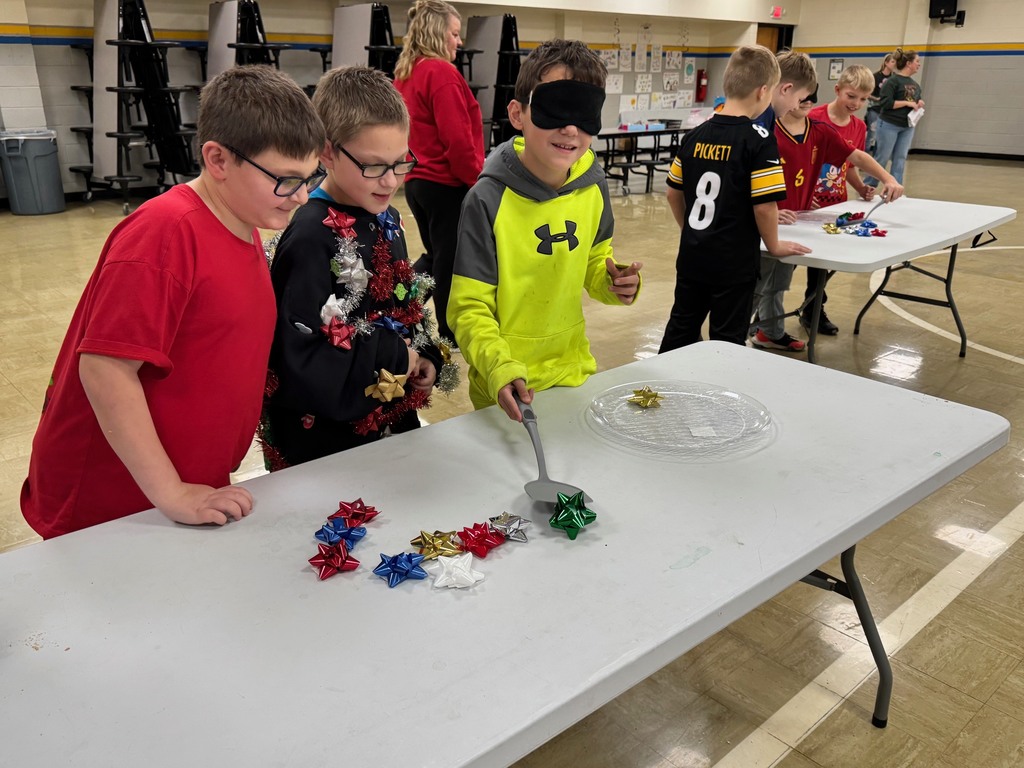 Students are blindfolded. They are holding a spatula and trying to find the bows and move them to the dish. 
