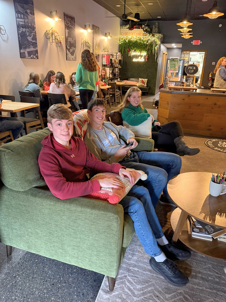 Students are sitting on a couch in a restaurant waiting for their food. 