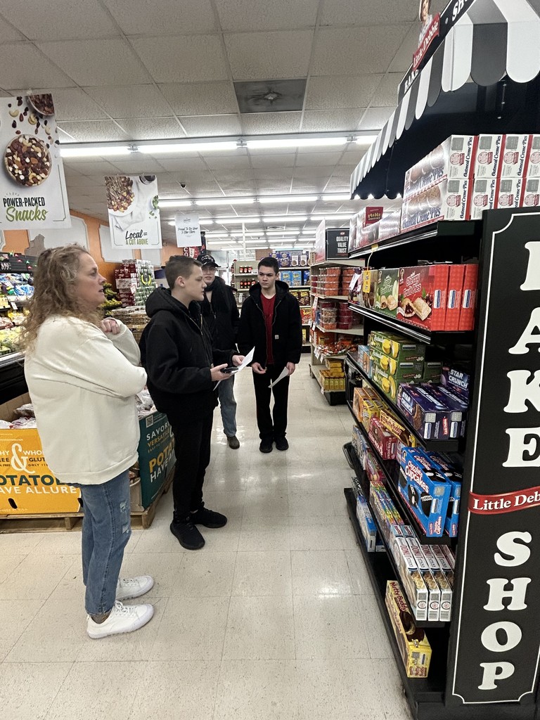 Three students and a teacher are looking for items on the shelves of the store. 