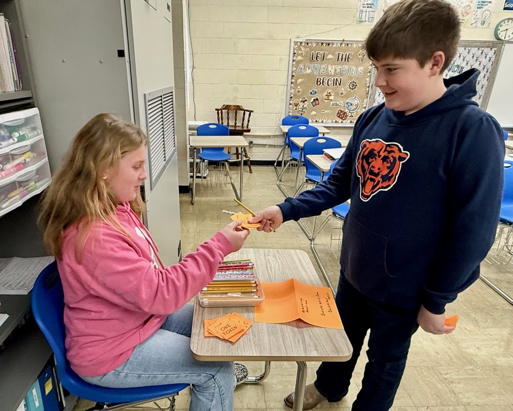 A student is at another student's desk buying a pencil.