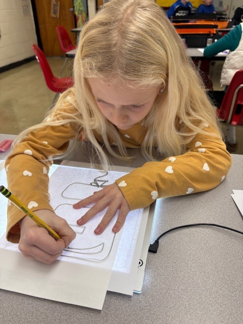 Students are tracing bubble letters using a light board. Their paper and the letter they are tracing on top of a board that is electronically lit up.