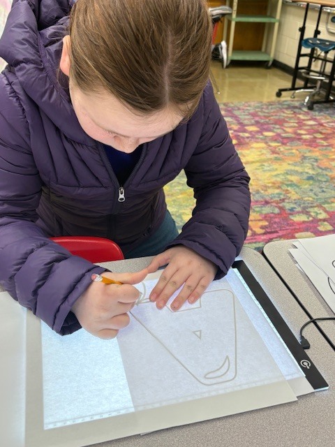 Students are tracing bubble letters using a light board. Their paper and the letter they are tracing on top of a board that is electronically lit up.