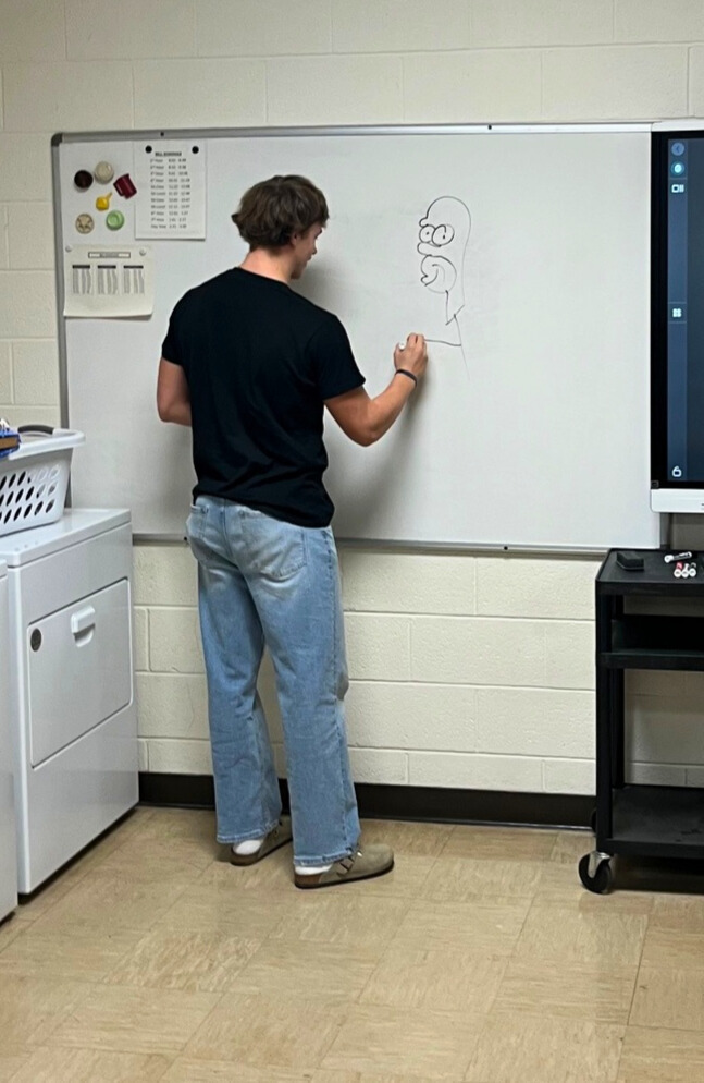 A student is standing at the white board. The student is drawing an object on the board. 