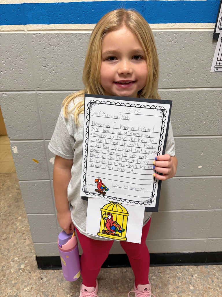 A student is standing in front of a wall. The student is holding her parent letter which is asking for a parrot. 
