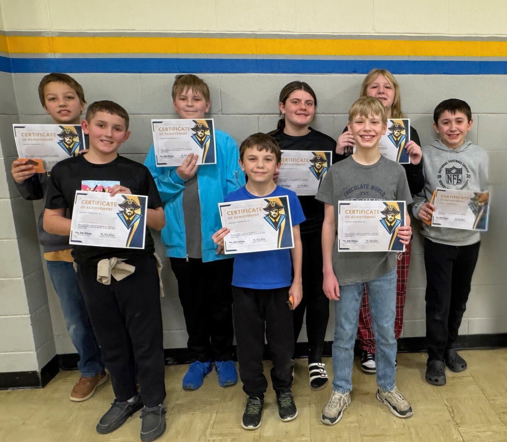 Students are in a group against the wall. They are holding up their perfect attendance certificates. 