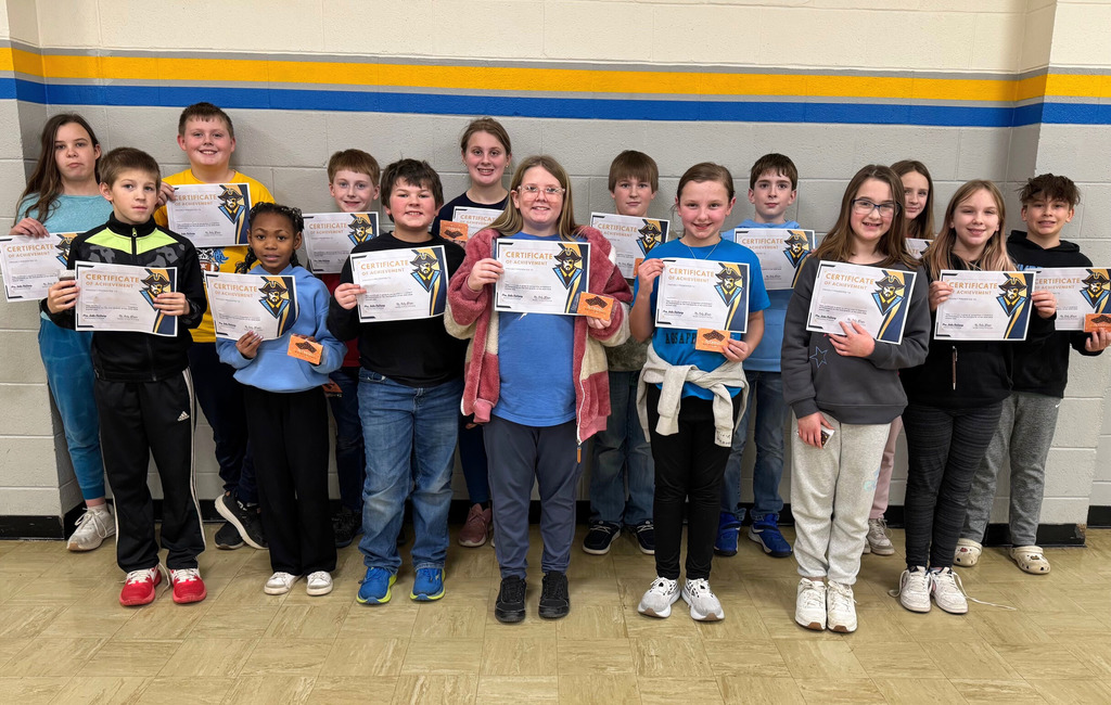 Students are in a group against the wall. They are holding up their perfect attendance certificates. 