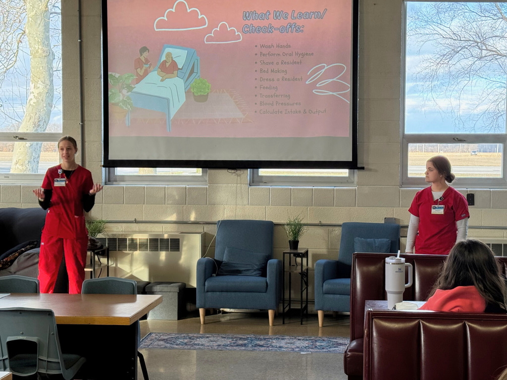 The two students are giving a presentation to fellow students about their expierences in Health Occ. Their is a presentation on the screen. 